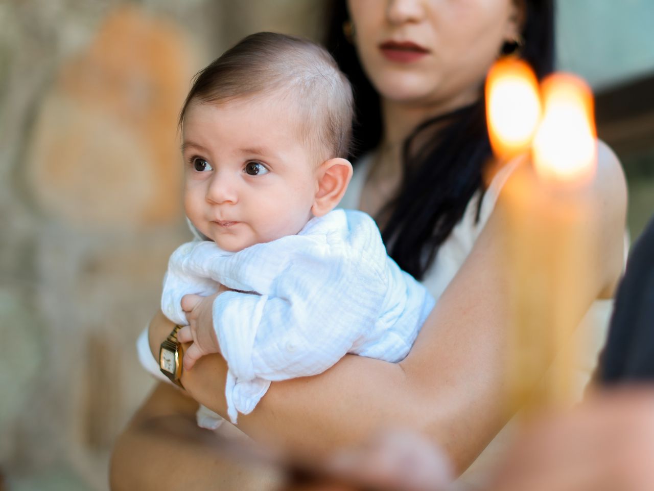 A mother lovingly holds her baby during a serene candlelit ceremony, capturing a tender moment.