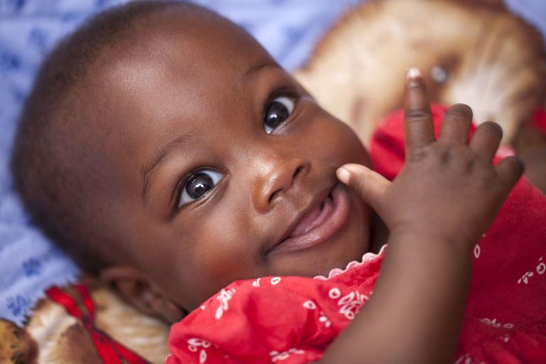 Close-up portrait of a happy baby smiling in a bright red outfit, showcasing joy and innocence.